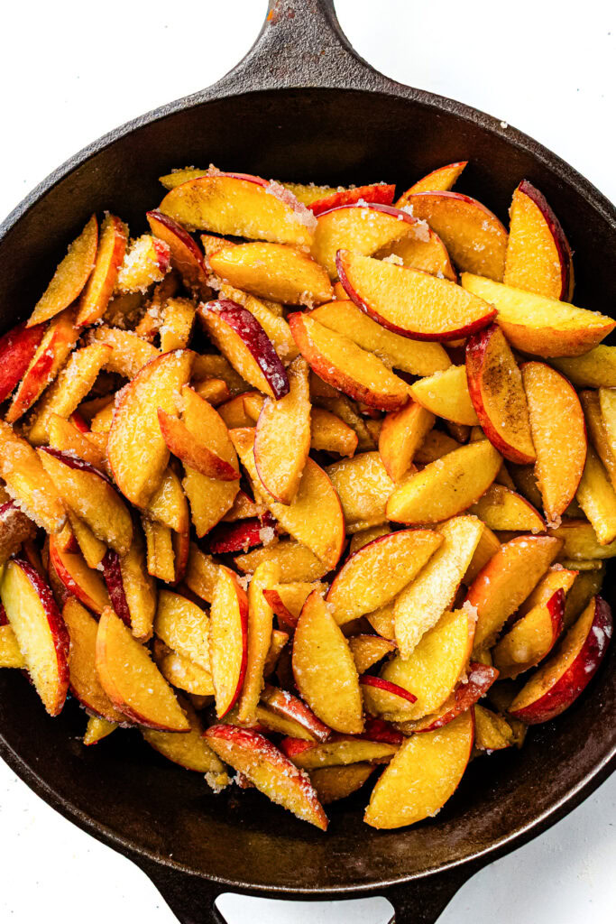 Sliced peaches coated with sugar in a cast iron skillet, ready to be cooked.