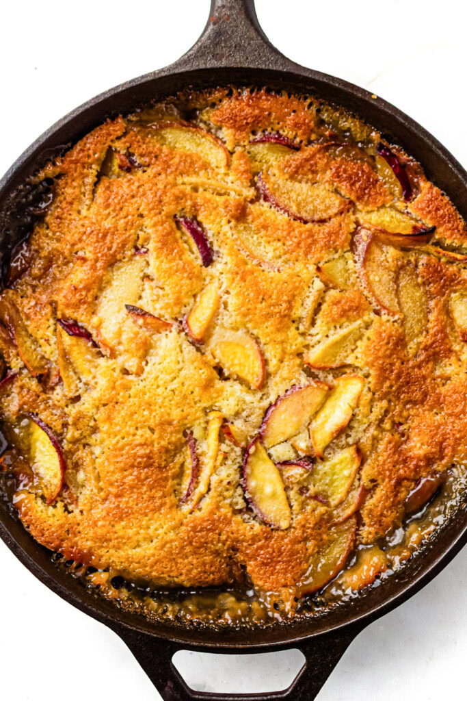 Golden peach cobbler baked in a cast iron skillet, with visible slices of peaches and a crispy browned crust.