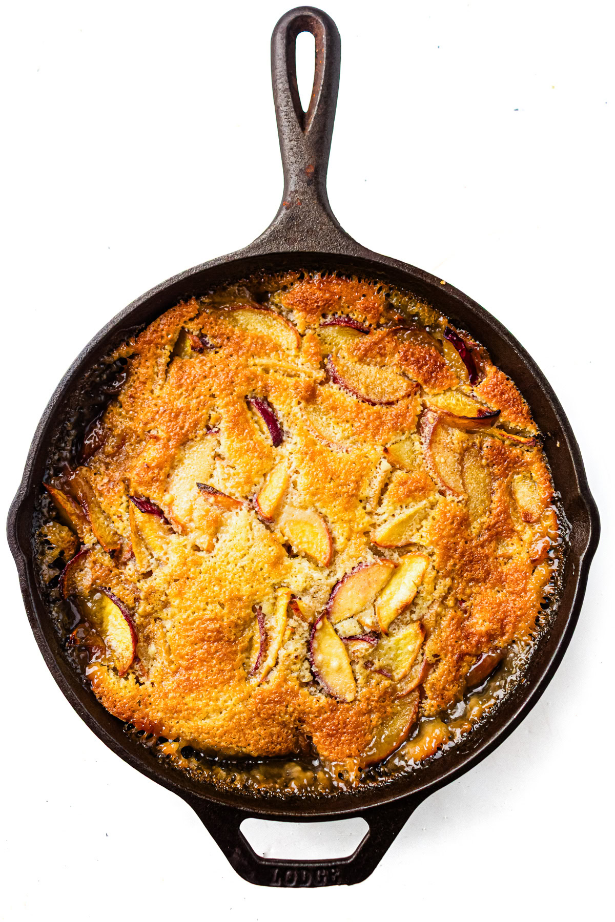 Golden-brown fruit cobbler with sliced peaches baked in a cast iron skillet, viewed from above.