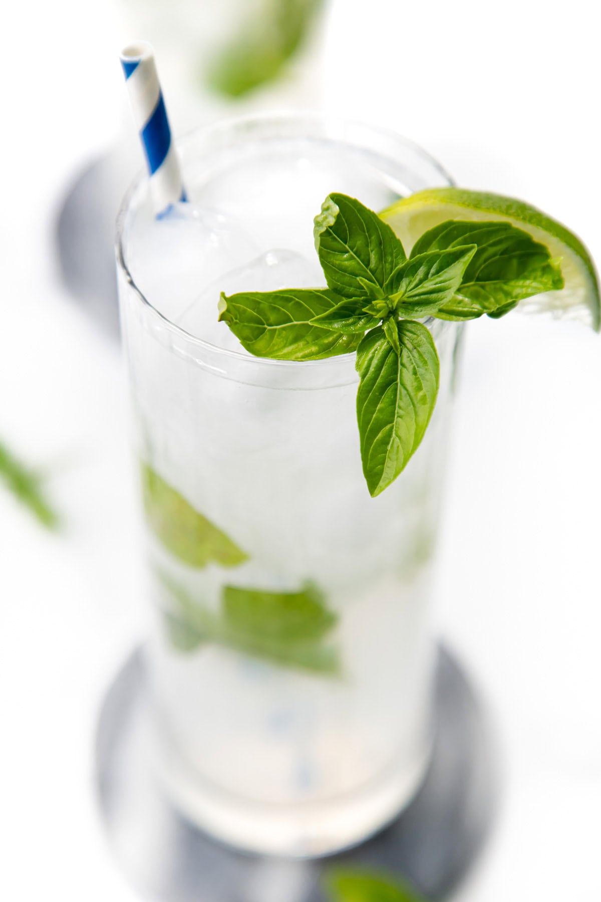 A mojito cocktail with ice, lime, mint leaves, and a blue-striped straw in a tall glass.