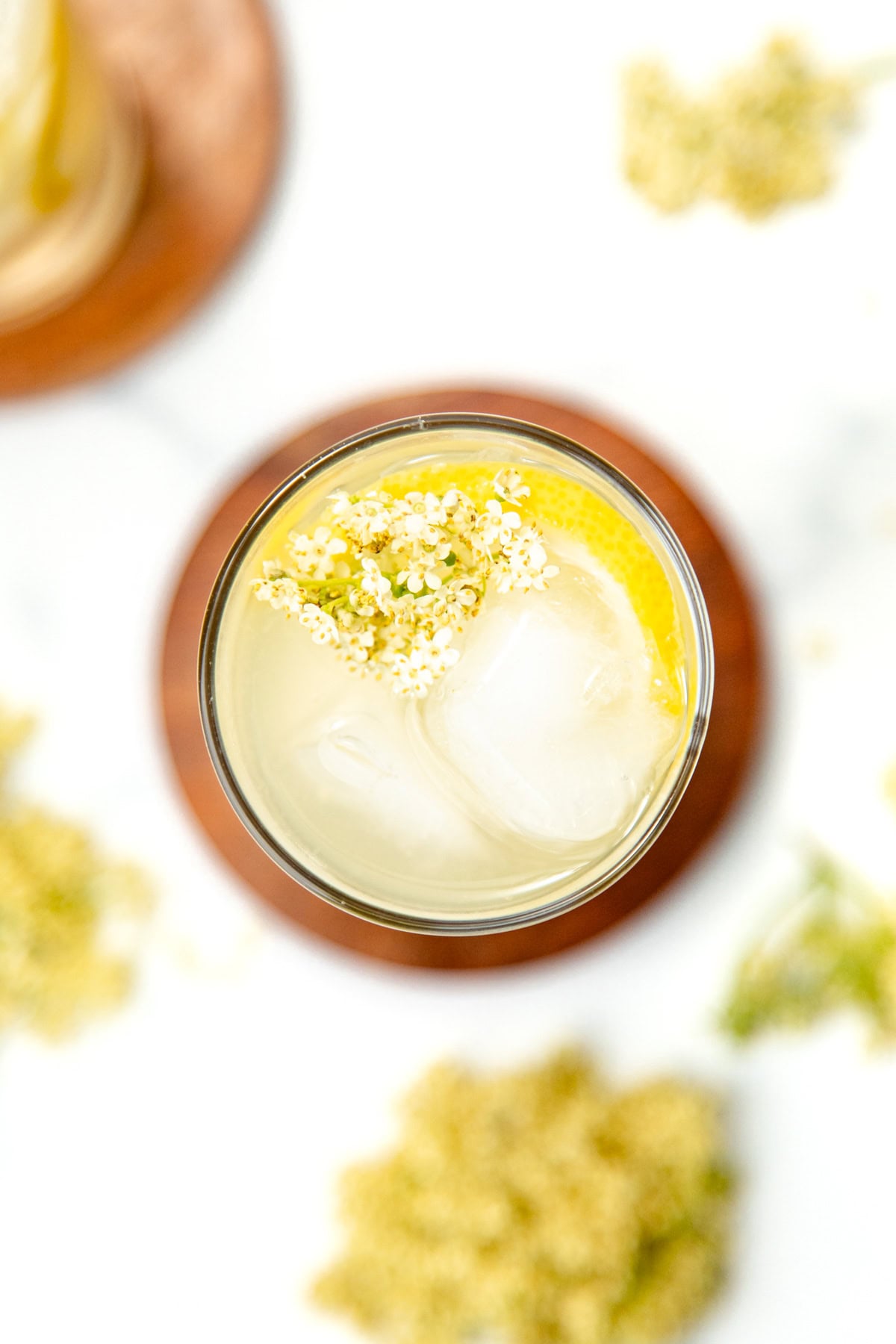 A glass of iced lemonade garnished with lemon slice and small white flowers, viewed from above.
