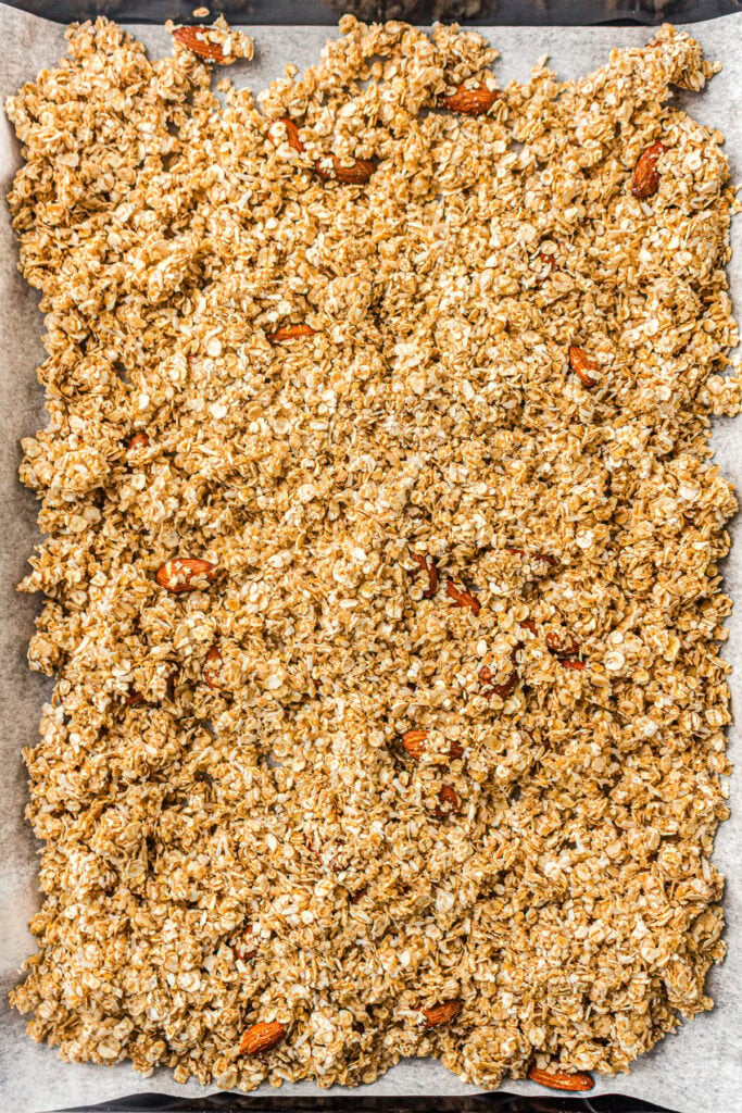 Granola mixture with oats and nuts spread on a parchment-lined baking sheet, ready for baking.