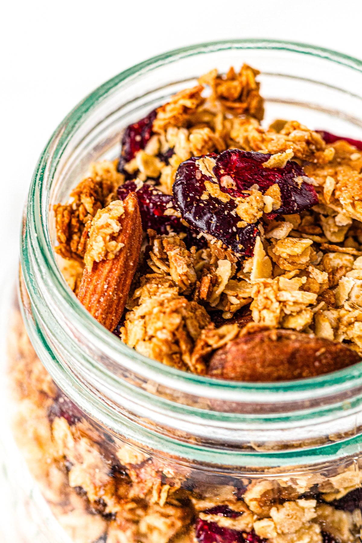 A jar filled with granola, almonds, and dried cranberries, viewed from above on a white background.