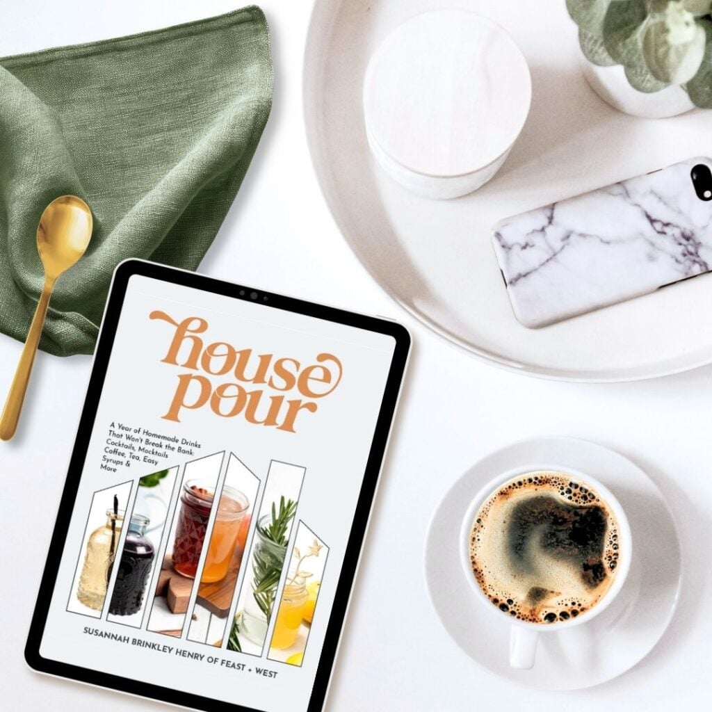 Tablet with "House Pour" book cover, coffee cup, phone, spoon, and napkin on a white surface—perfect for planning your next bar promotion or discovering the latest drink offer.
