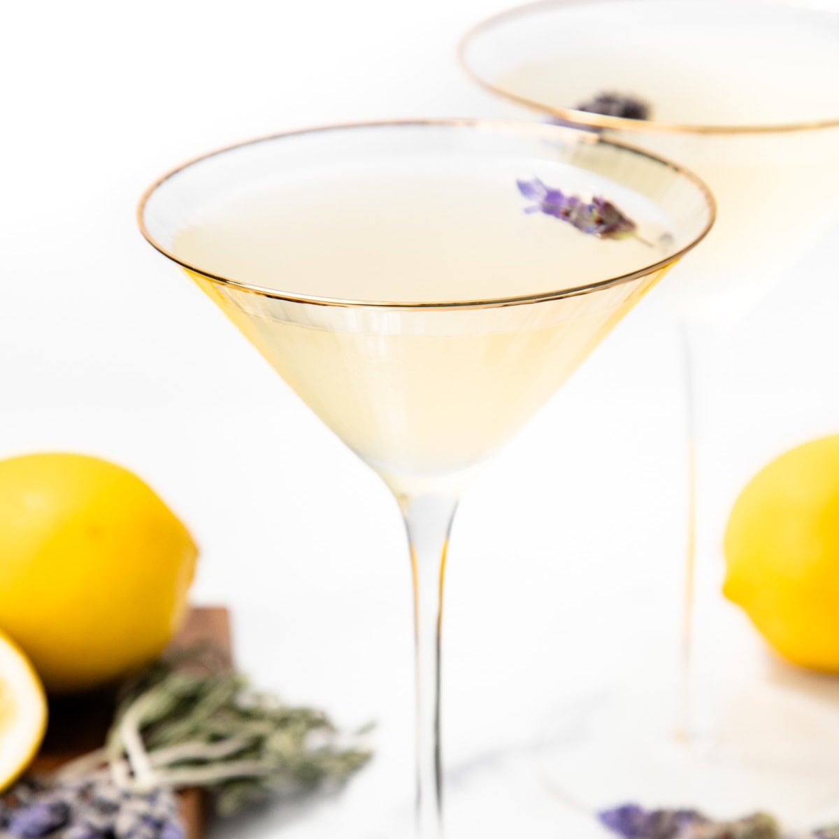 Martini glass with pale yellow drink, garnished with lavender; lemons and lavender sprigs nearby.