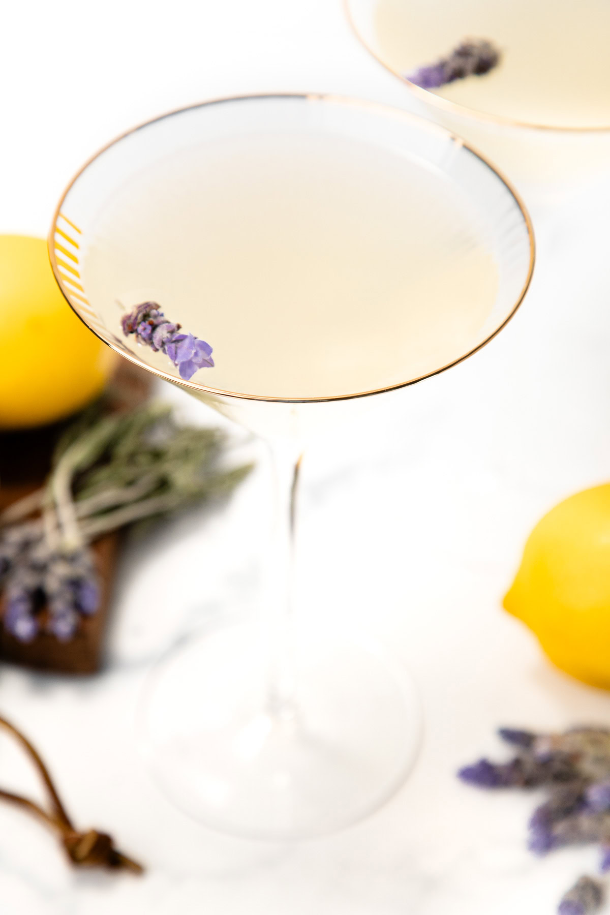 A cocktail in a martini glass garnished with lavender, surrounded by lemons and lavender sprigs.