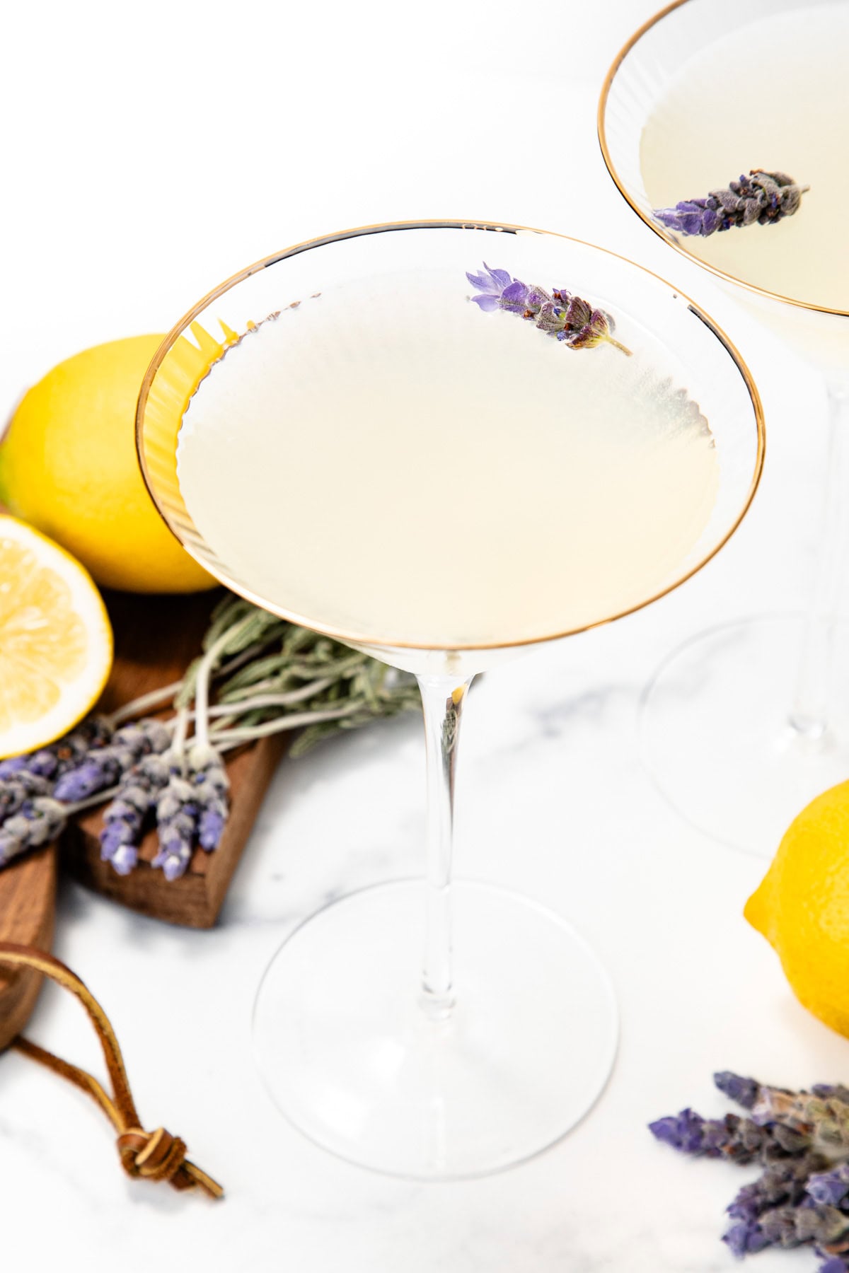 A martini glass with a pale drink, garnished with lavender, surrounded by lemons and lavender sprigs.