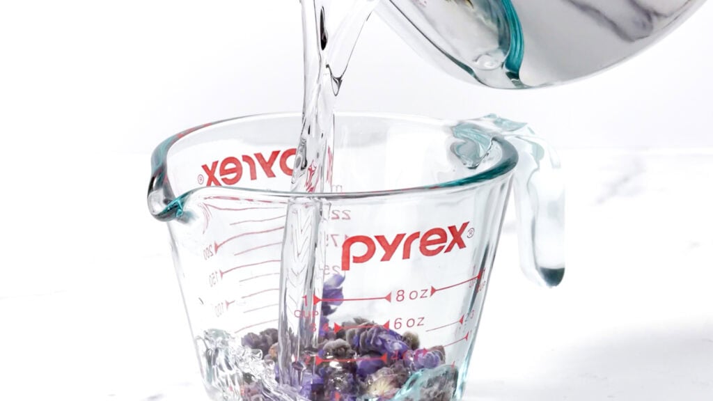 Water is being poured into a Pyrex measuring cup filled with beads on a white background.