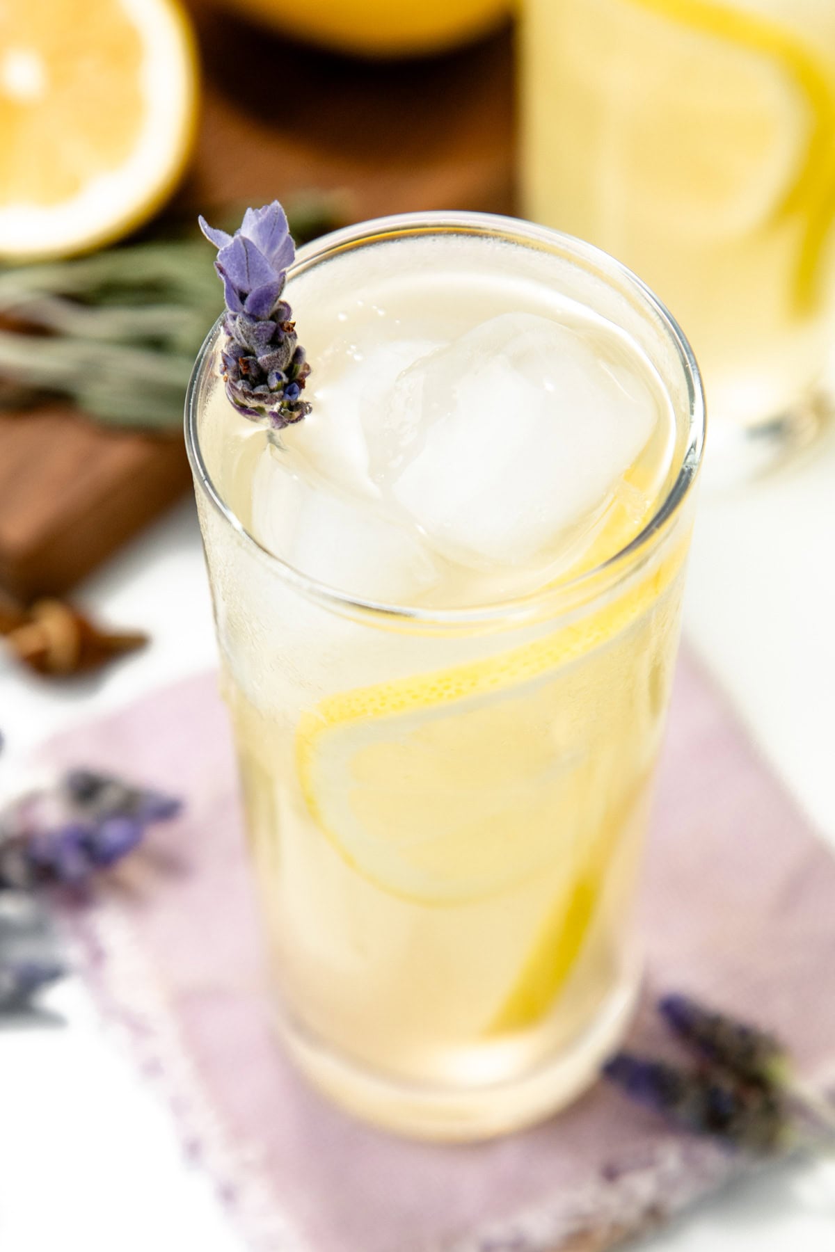 A glass of iced lemonade with a lemon slice and a sprig of lavender on a light purple napkin.