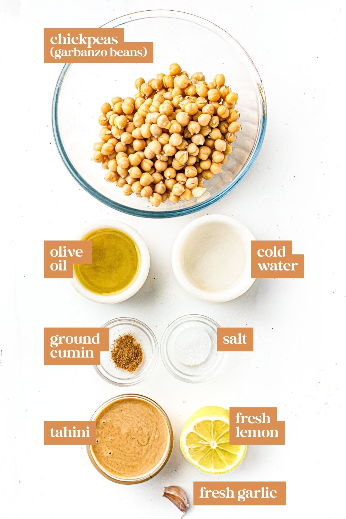 Ingredients for hummus: chickpeas, olive oil, water, cumin, salt, tahini, lemon, and garlic, arranged in bowls.