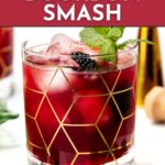 A glass of blackberry bourbon smash with ice, mint, and gold geometric lines on the glass.