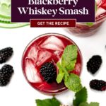 Overhead view of a red blackberry cocktail with ice, mint garnish, and fresh blackberries on a white surface.