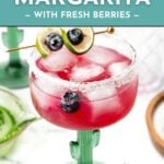 A blueberry margarita in a cactus glass, garnished with lime and blueberries, with ice and a sugared rim.