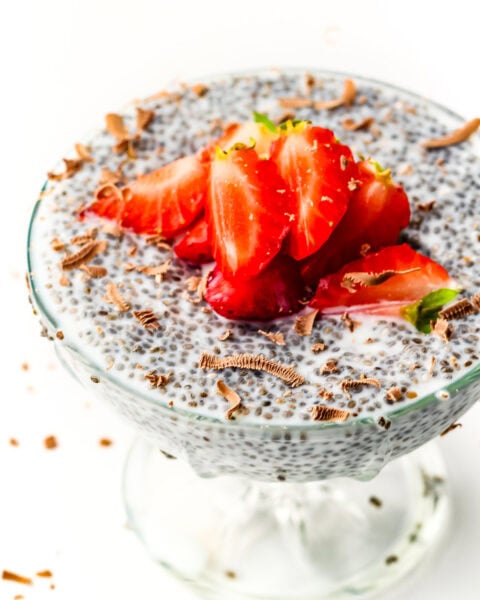Chia pudding in a glass dish topped with sliced strawberries and chocolate shavings on white background.