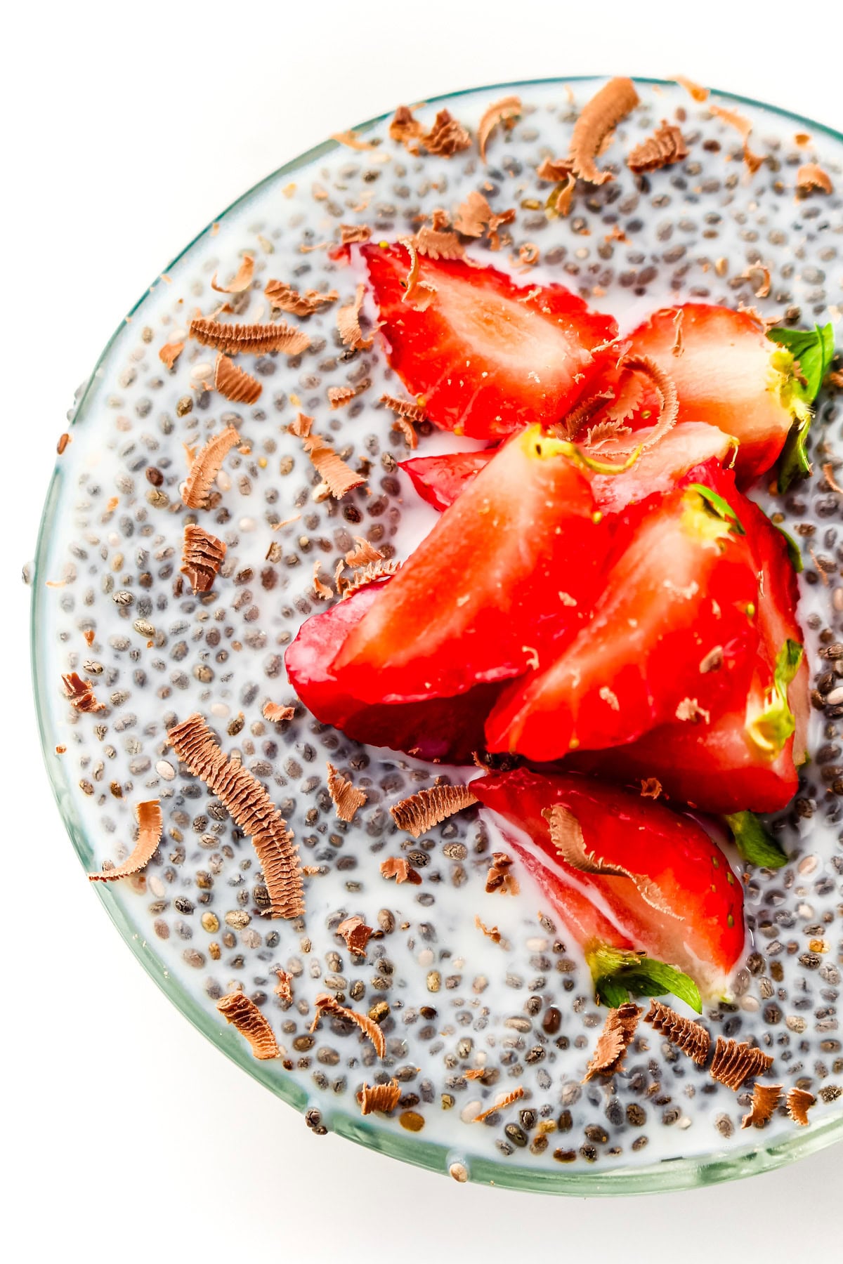 Chia pudding with milk, topped with sliced strawberries and chocolate shavings in a glass bowl.