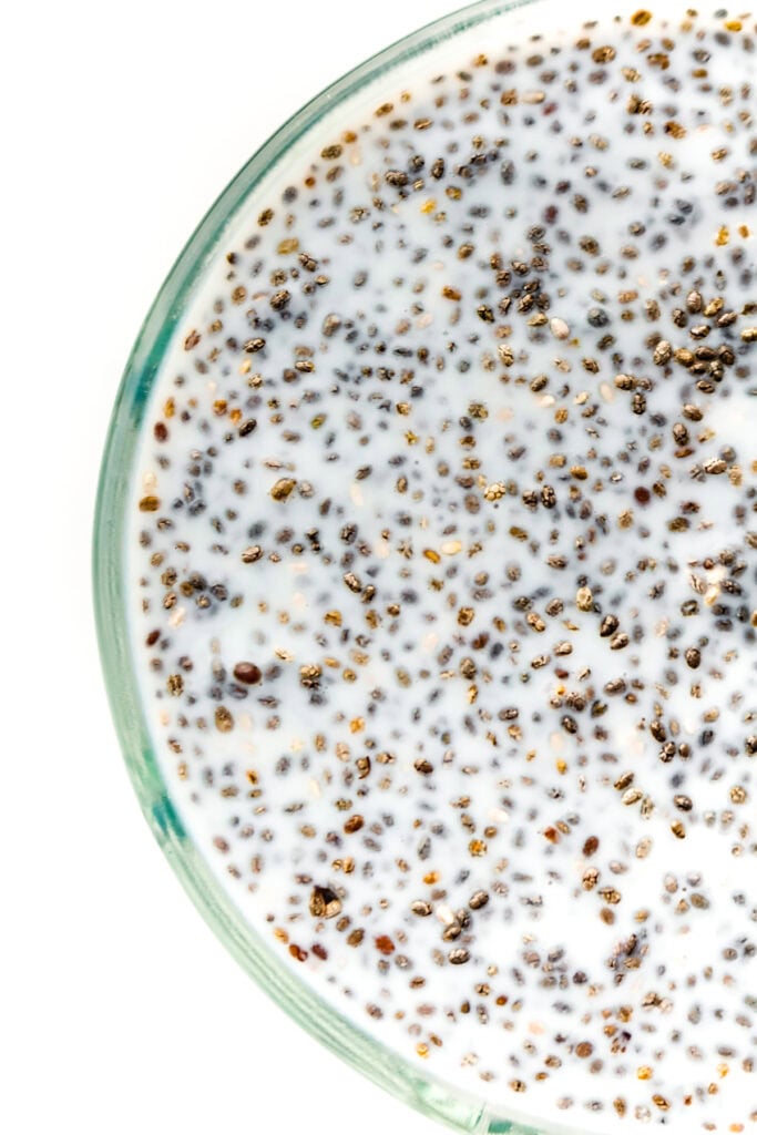 Close-up of a glass bowl filled with chia seeds soaked in milk, shot from above on a white background.