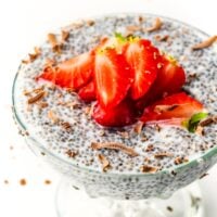 Chia pudding in a glass, topped with sliced strawberries and chocolate shavings on a white background.