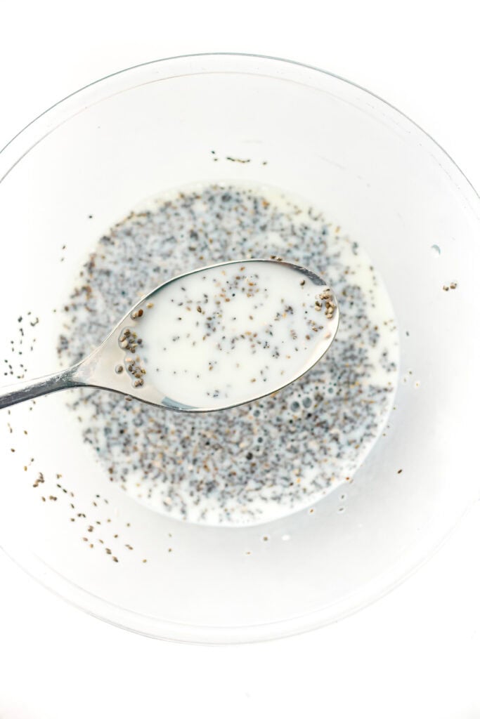 A spoon holds milk and chia seeds over a bowl with more milk and chia seeds.