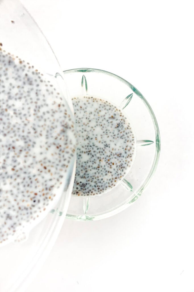 A close-up of chia seed pudding in a glass bowl, viewed from above on a white background.