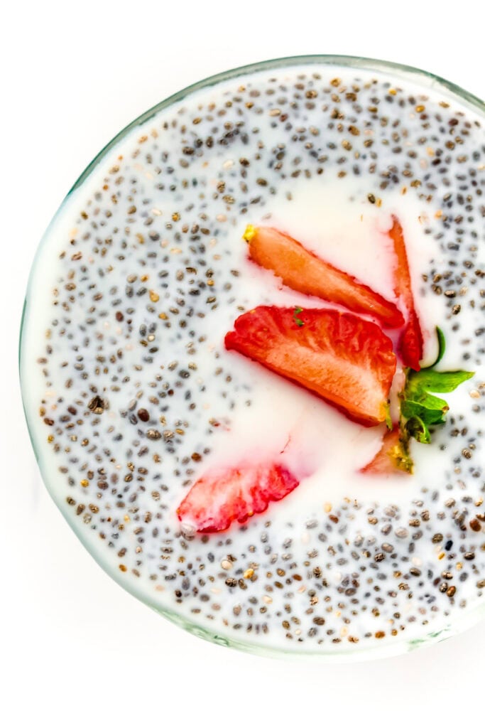 A bowl of chia pudding topped with sliced strawberries, photographed from above on a white background.