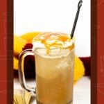 A glass mug of frozen butterbeer topped with foam and caramel drizzle, with a straw and themed props.