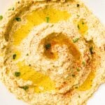 Creamy hummus topped with olive oil, paprika, and chopped parsley on a white plate.