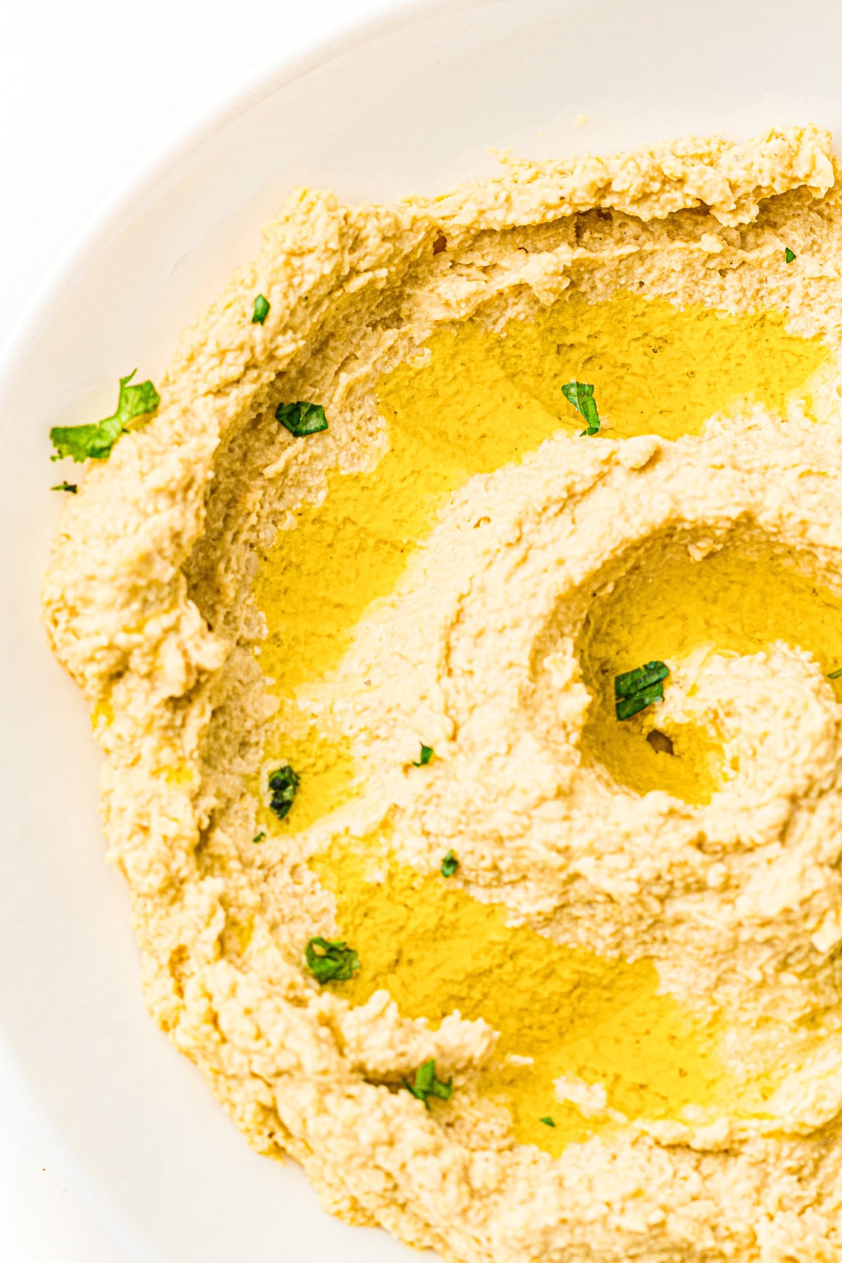 Bowl of hummus drizzled with olive oil and garnished with chopped herbs.