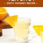 A clear glass of orange tea shot garnished with an orange slice, with orange wedges in the background.