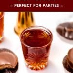 A glass of brown liquid sits with peanut butter cups, gold shot glass, and party decor in the background.