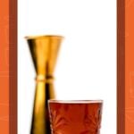 A chocolate peanut butter cup shot in a decorated glass with a gold jigger in the background.