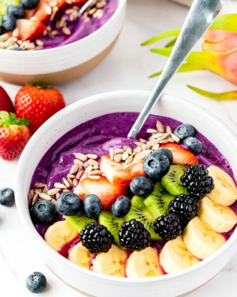 A smoothie bowl topped with banana, kiwi, blackberry, blueberry, strawberry, and sunflower seeds.