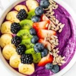 Smoothie bowl topped with banana, kiwi, blackberries, blueberries, strawberries, and sunflower seeds.