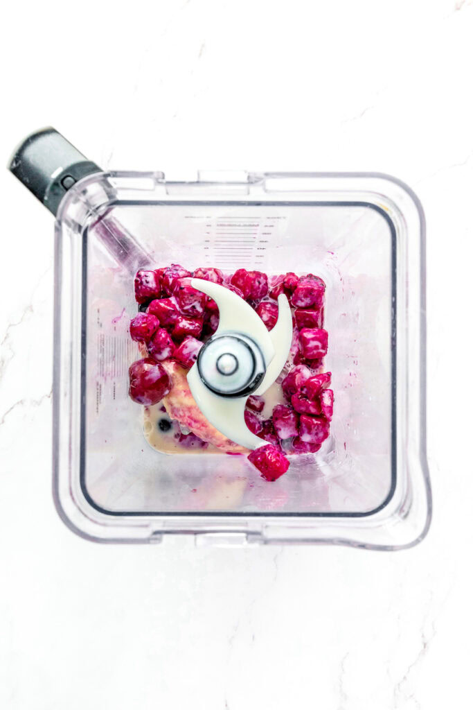 Frozen berries, banana, and milk inside a blender viewed from above, ready to be blended.