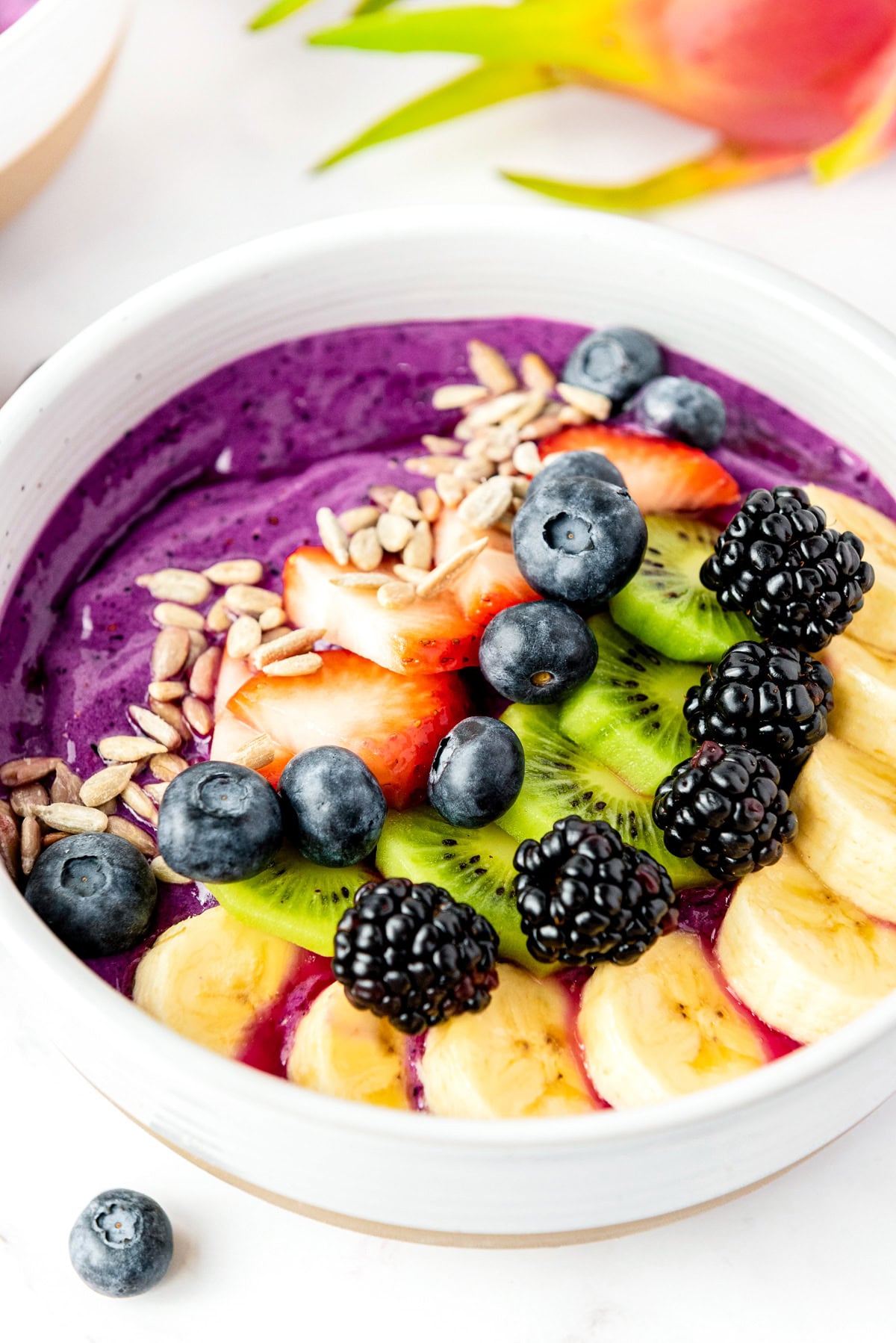 A smoothie bowl topped with banana, kiwi, blackberry, strawberry, blueberry, and sunflower seeds.