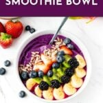 A dragon fruit smoothie bowl topped with banana, kiwi, berries, seeds, and a spoon on a white table.