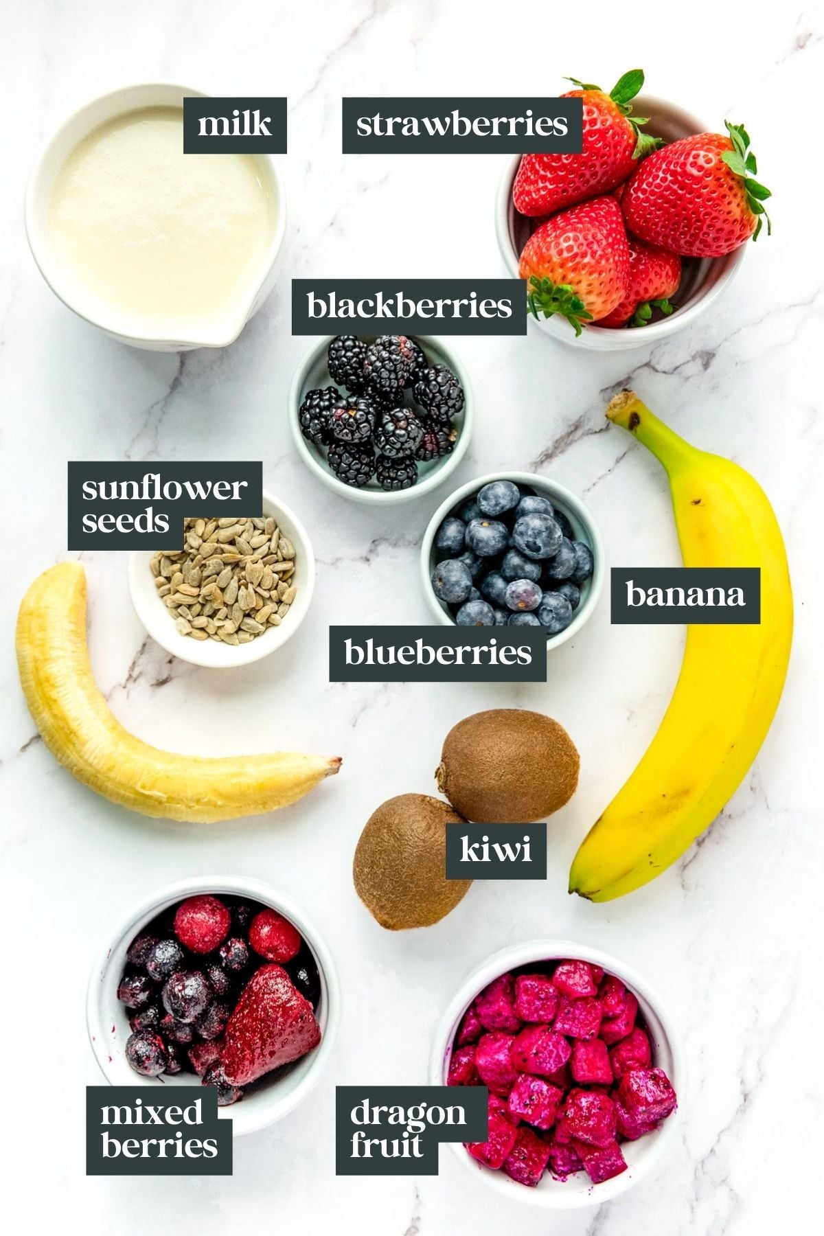 Bowls of milk, strawberries, blackberries, sunflower seeds, blueberries, banana, kiwi, mixed berries, dragon fruit.