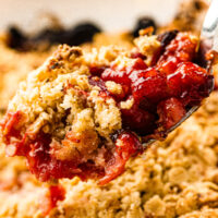 A spoonful of strawberry crumble with golden oat topping and juicy red fruit filling.