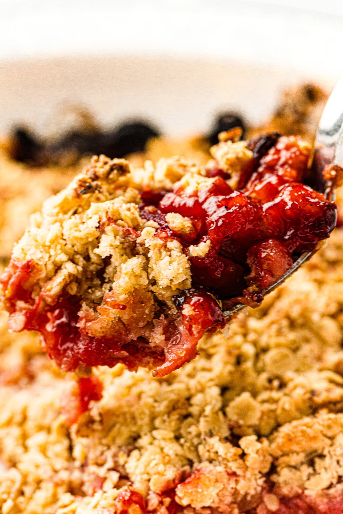 A spoonful of strawberry crumble with golden oat topping and juicy red fruit filling.