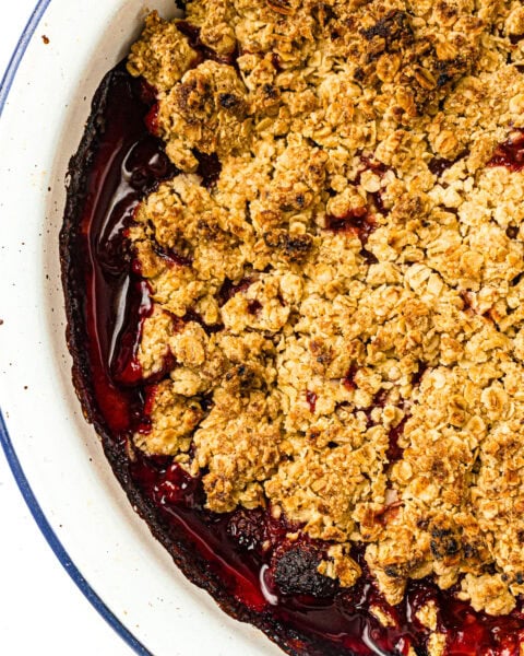 Baked berry crumble with golden oat topping in a white dish, edges showing juicy red filling.
