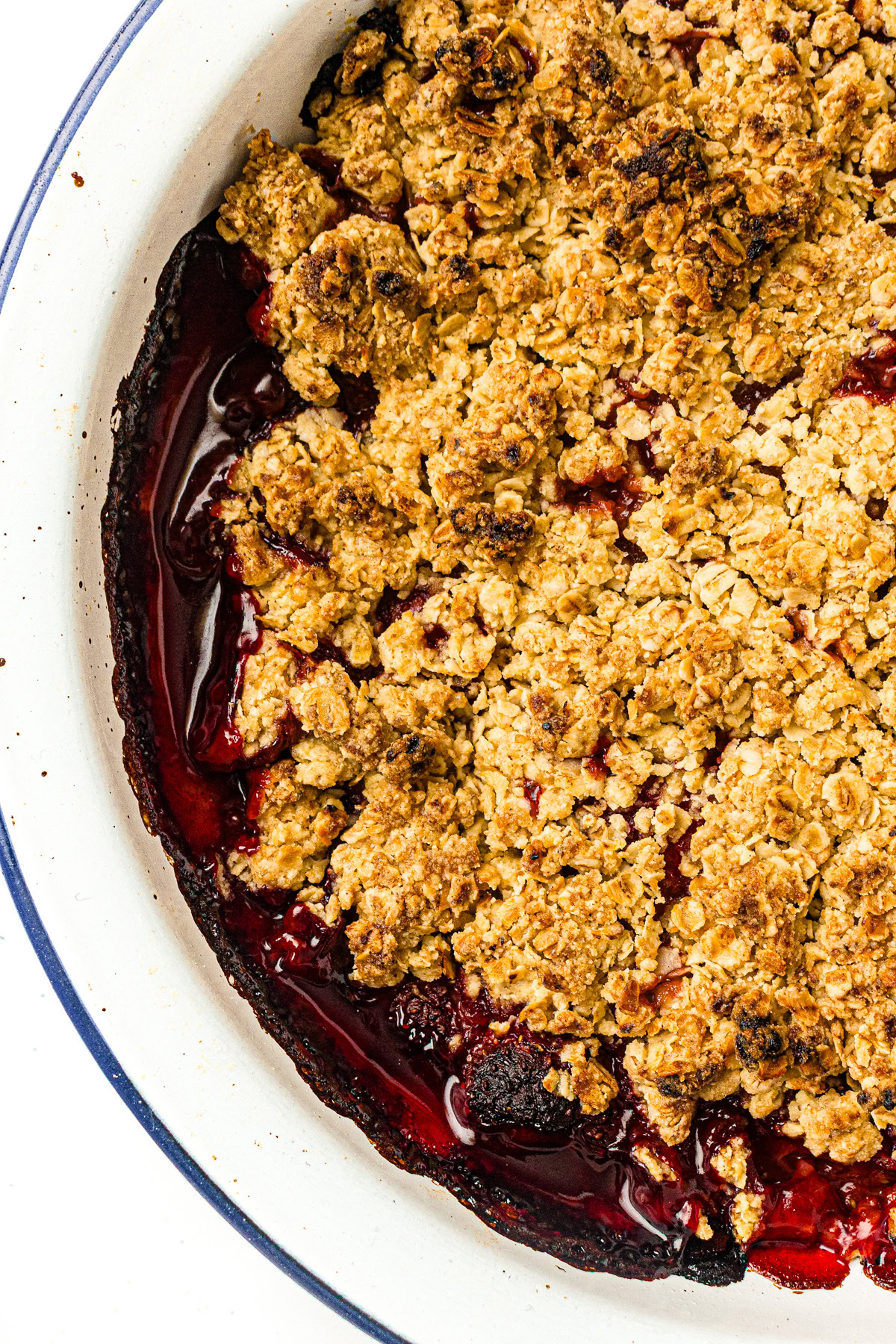 Baked berry crumble with golden oat topping in a white dish, edges showing juicy red filling.
