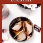 Overhead view of a cocktail with ice, brown liquid, and a straw, surrounded by Tootsie Roll candies.