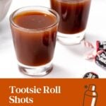 Two glasses with brown Tootsie Roll shots on a white table, with Tootsie Roll candies in the background.
