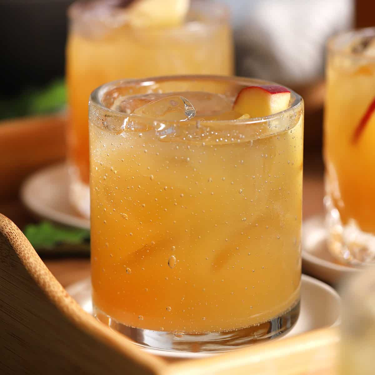 A glass of iced apple cider garnished with apple slices sits on a small white plate.