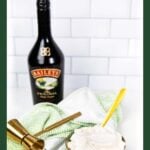 A bottle of Baileys, a green bowl of whipped cream, gold spoon, and bar tools on a green towel.