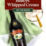 Baileys bottle next to a bowl of whipped cream with spoons and a green patterned towel on a white surface.