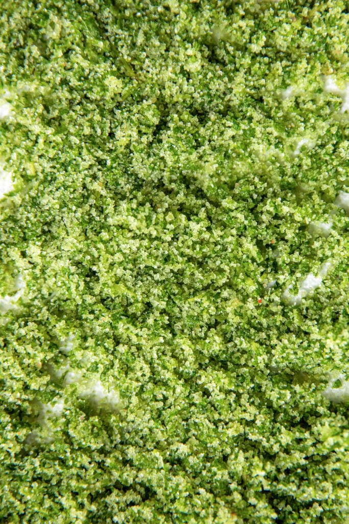 Close-up of finely chopped green herbs or vegetables scattered over a white surface.