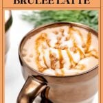 A caramel brûlée latte in a metallic mug topped with whipped cream, caramel drizzle, and crushed toffee.