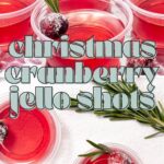 Plastic cups with red cranberry jello shots, garnished with rosemary and sugared cranberries.