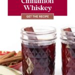 Two jars of cinnamon whiskey with cinnamon sticks, a lid, and whole cinnamon sticks on the side.