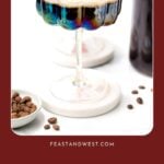 Two colorful cocktails in vintage glasses on a white surface with coffee beans, bottle, and recipe invitation.